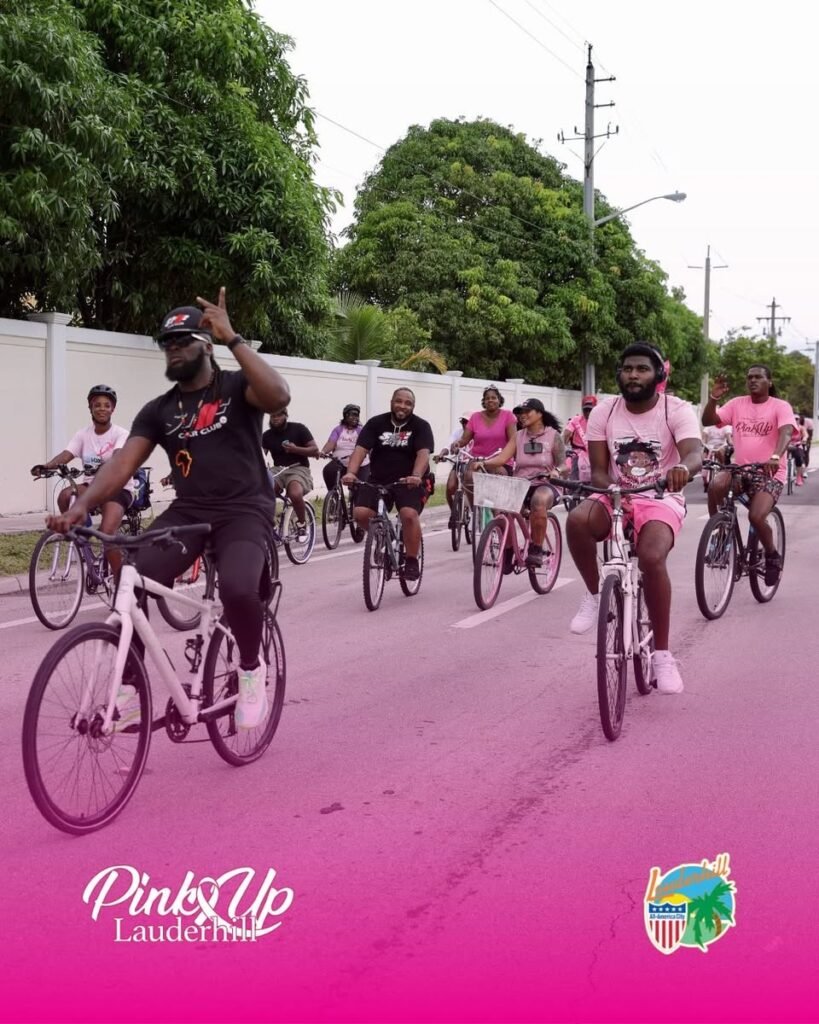 Group of cyclists wearing pink and black clothing riding bicycles along a Lauderhill street during a Pink Up Lauderhill breast cancer awareness event.